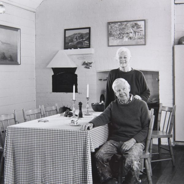 Black and white photo of 2 people standing beside a table in an old kitchen