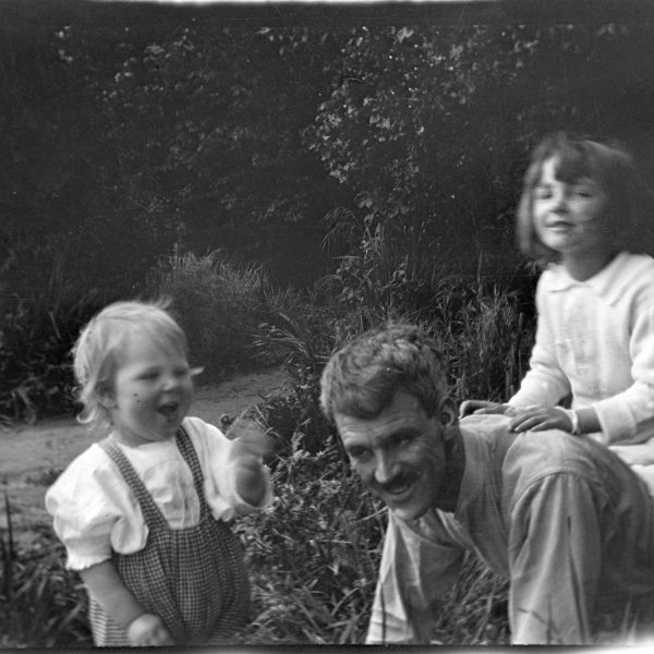 Photograph of a man and two young children playing outside