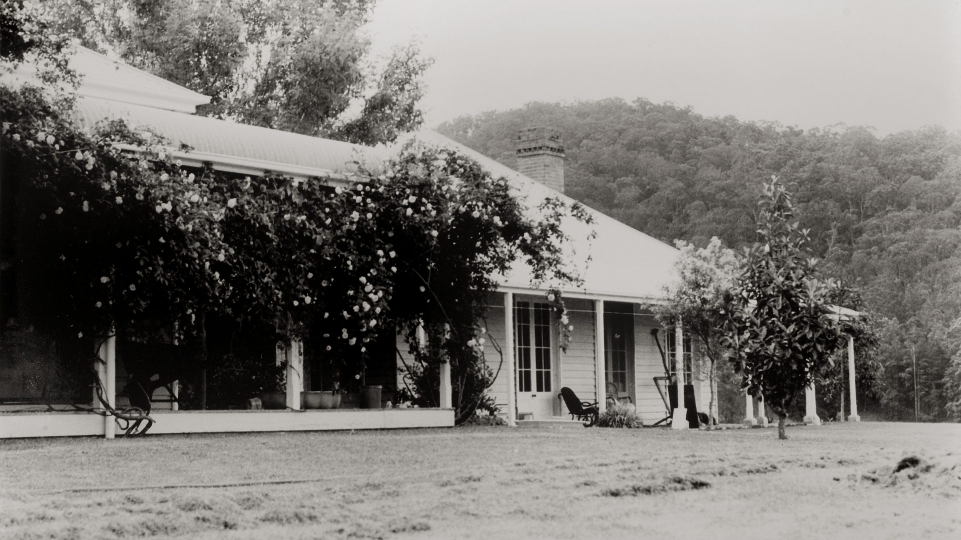 Black and white photo of an old house and a river and mountains in the background