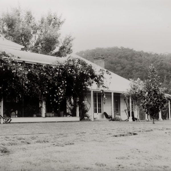 Black and white photo of an old house and a river and mountains in the background