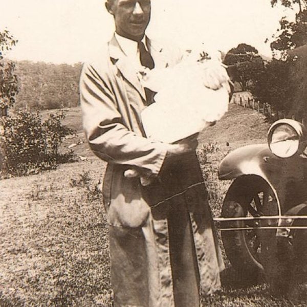 Old photo of a man holding a baby beside a car