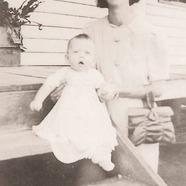 Woman standing beside a home veranda with a baby