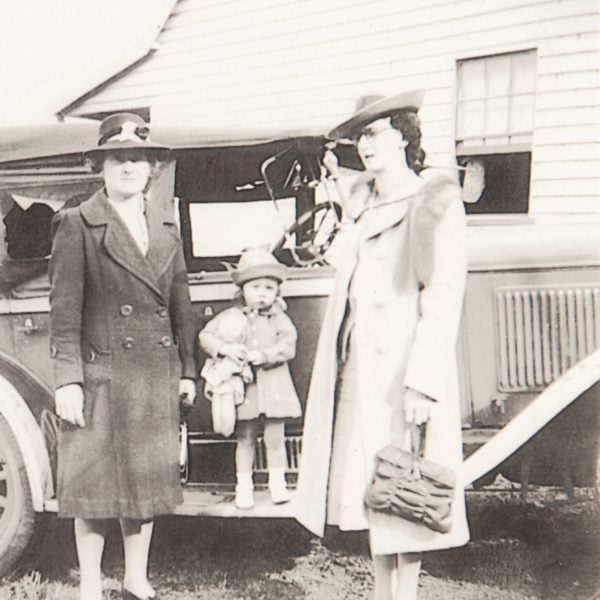 Old photo of two women standing with a child next to a car