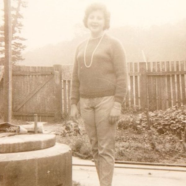 Old photo of a woman standing beside a brick well