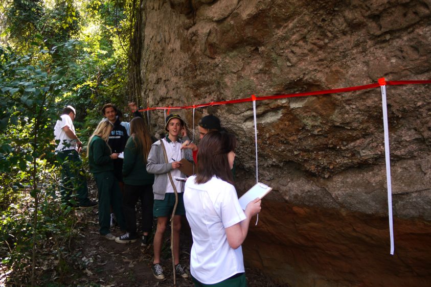 Students stand in front of a large rockface that has tape on it