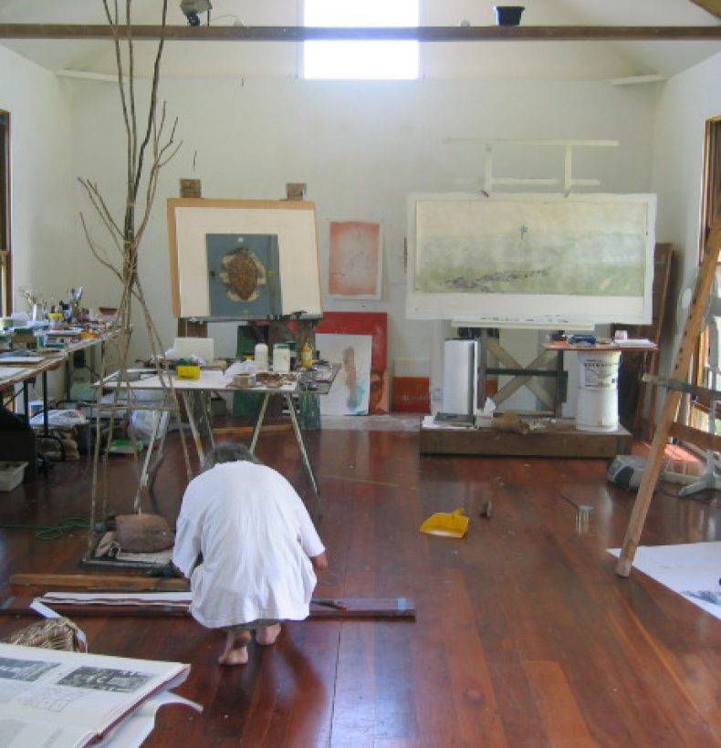 Person crouched over in an art studio with easels and large paintings in the room