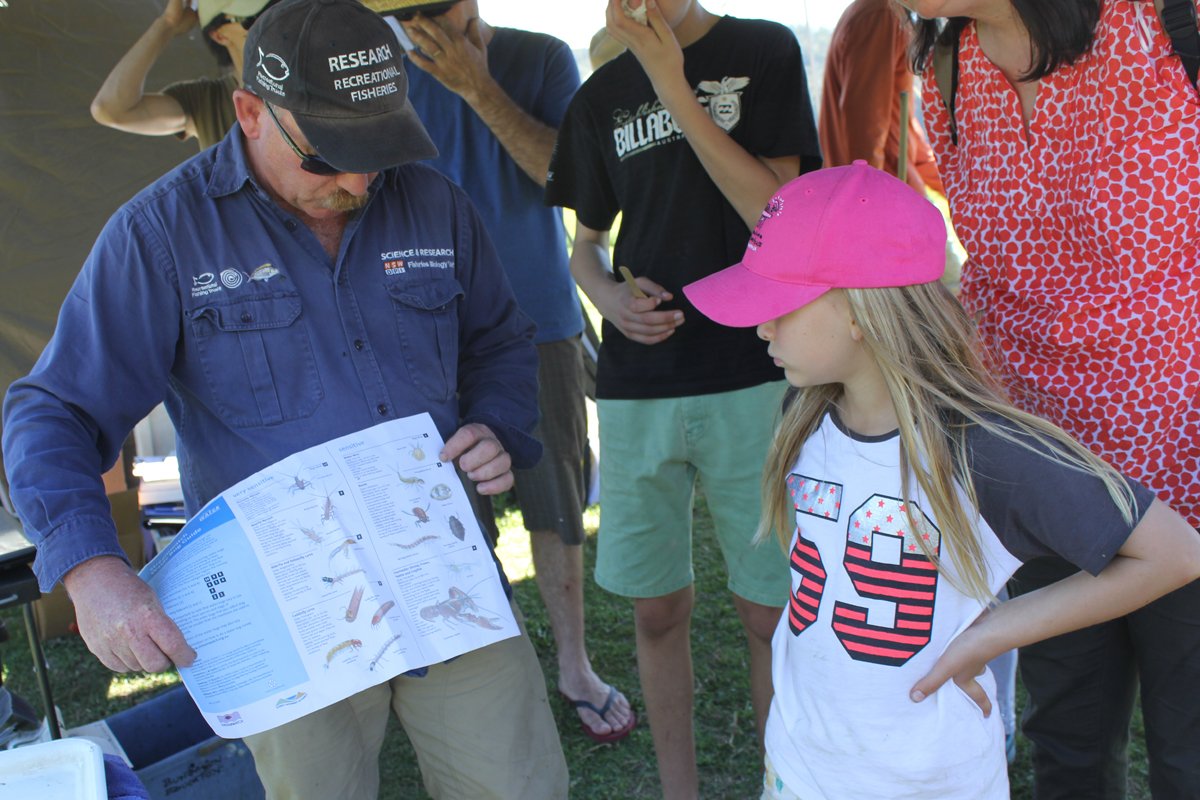 Man stands holding a chart showing different fish species to a young child