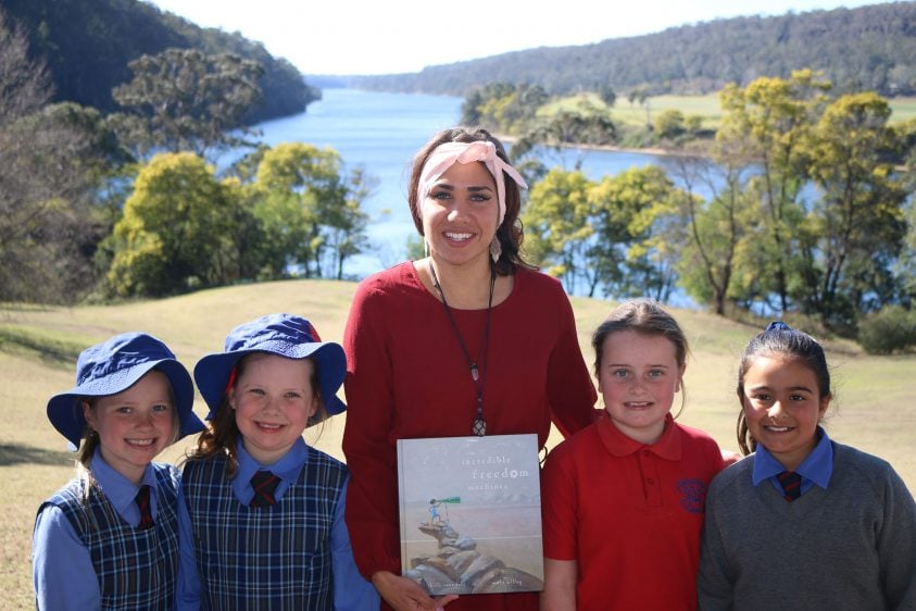 4 children stand with an adult who is holding a book