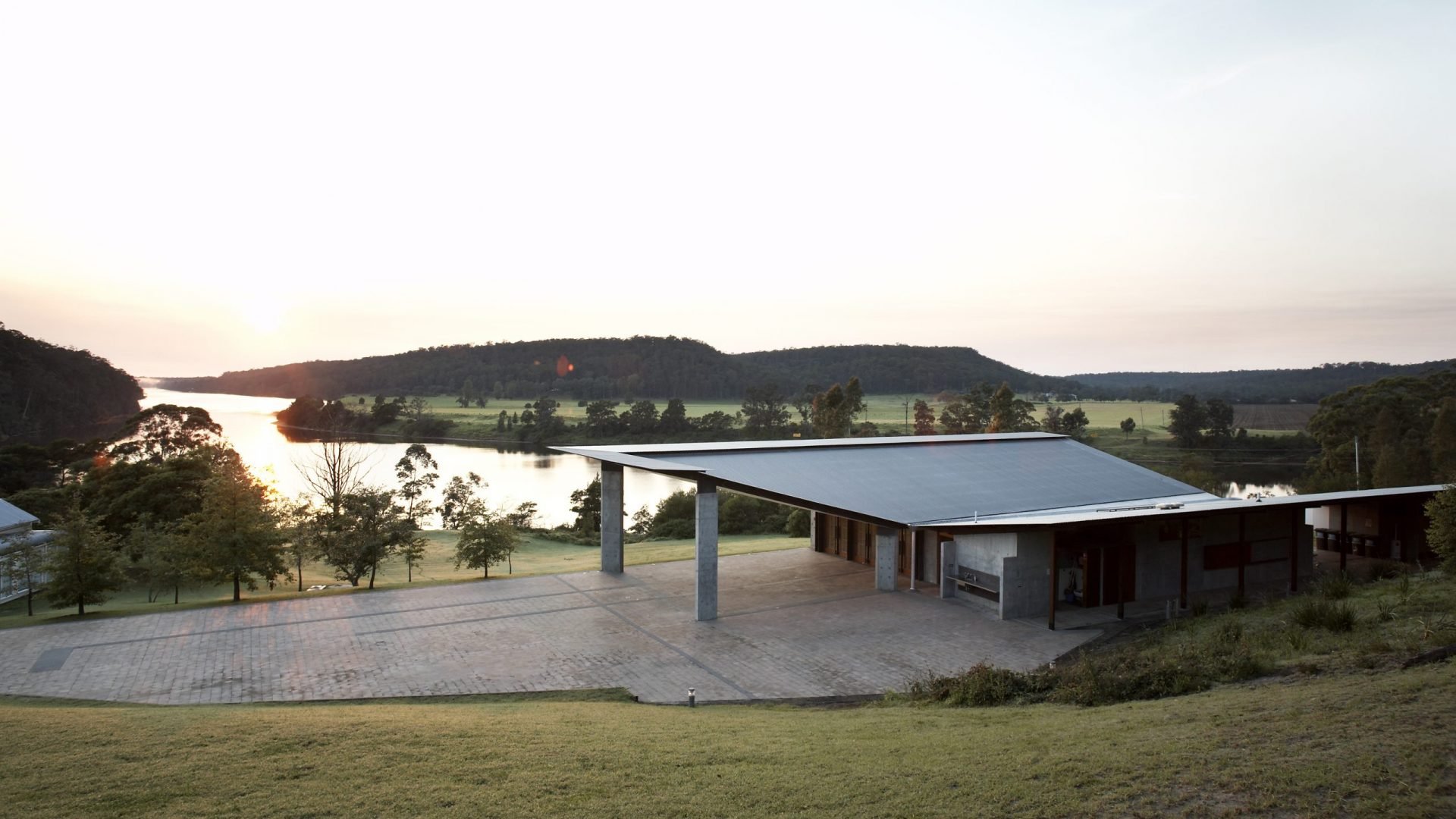 A contemporary building with a large forecourt. A river and mountains are in the background.