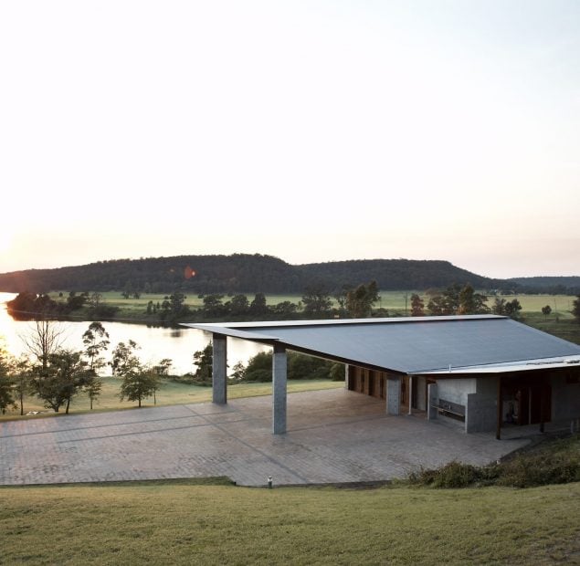 A contemporary building with a large forecourt. A river and mountains are in the background.