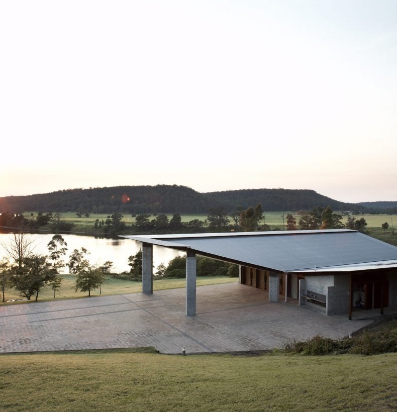 A contemporary building with a large forecourt. A river and mountains are in the background.