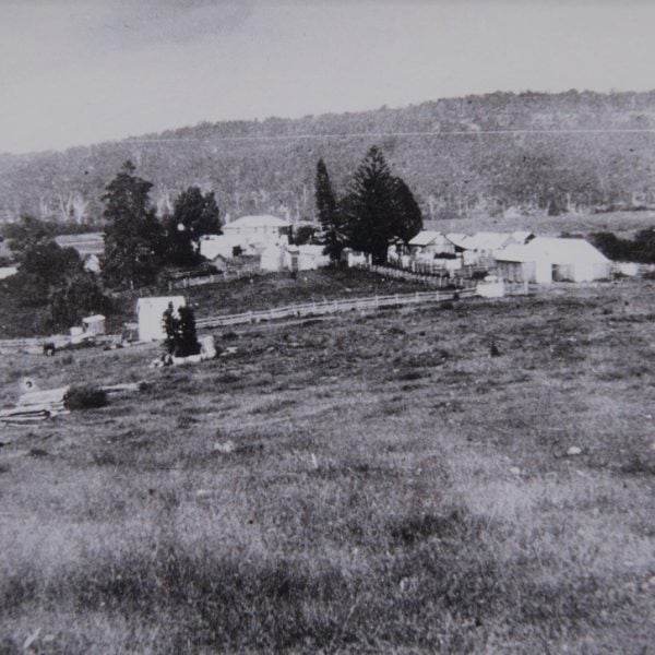 Black and white photo of farm buildings in a field surrounded by mountains