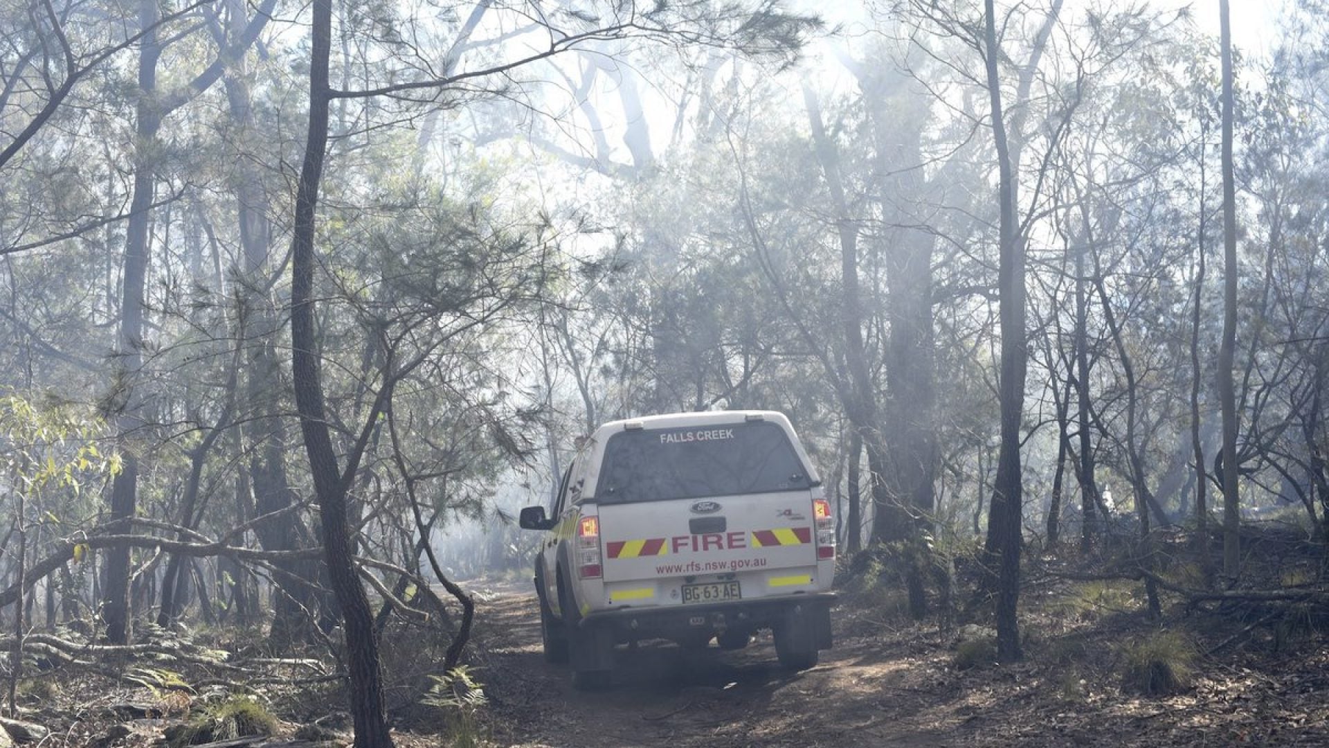 A rural fire services car drives down a dirt track through a smokey landscape