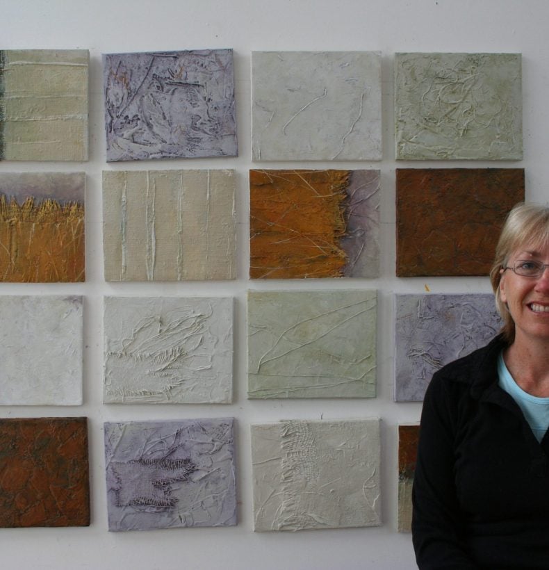 Person standing in front of 16 small abstract paintings hanging on a wall