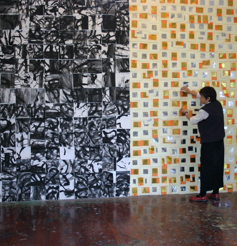 Person touching a wall covered in small orange and gold pieces of paper