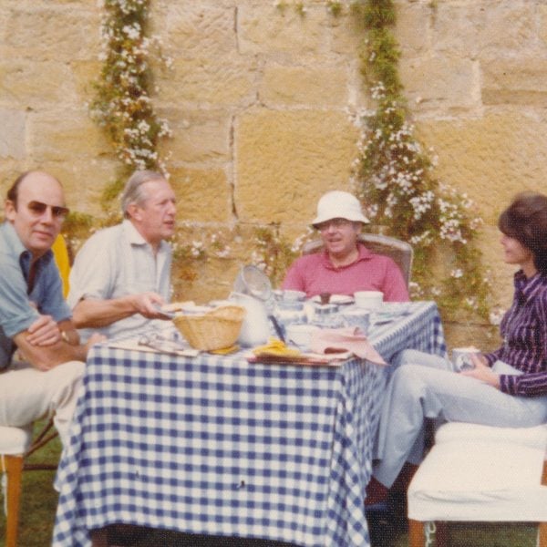 Three men and a women sitting at a table outside a sandstone building