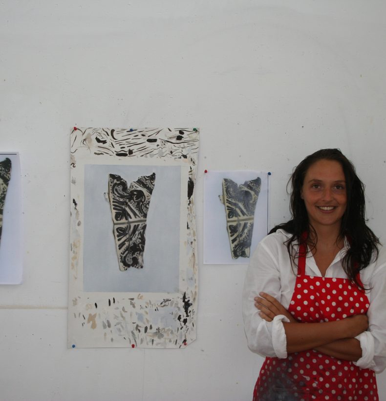 Person standing in front of a wall with artworks pinned to it. Person wearing a red apron