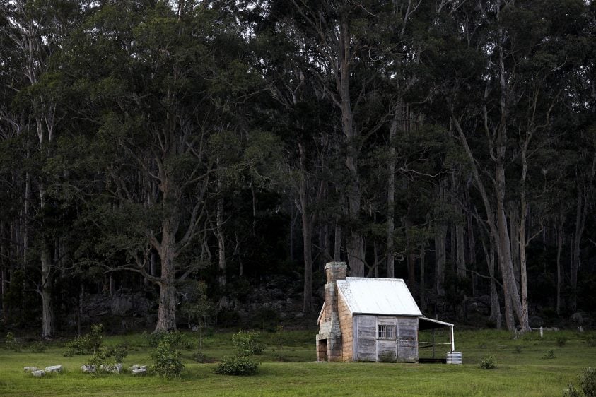 A small wooden cottage alongside bushland and green grass