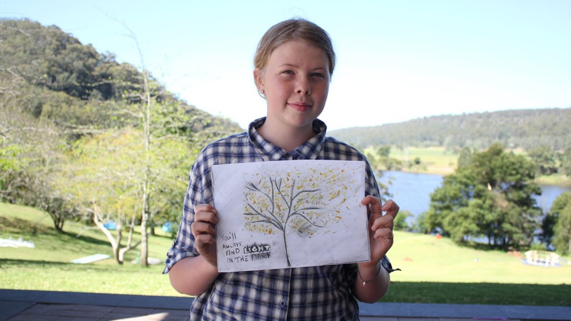 A child holds up a painting of a tree with the words