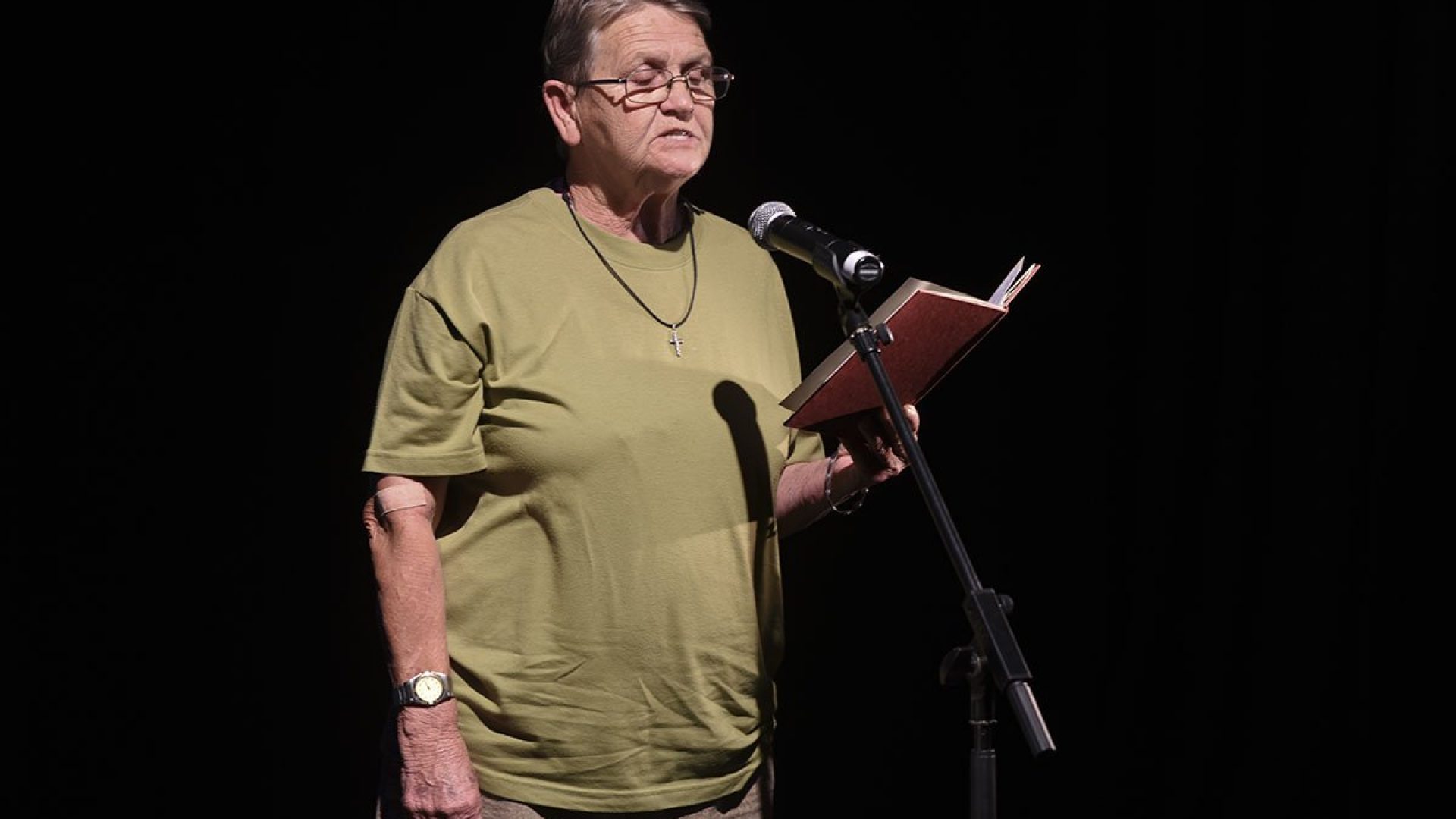 A person standing at a microphone, reading from a book