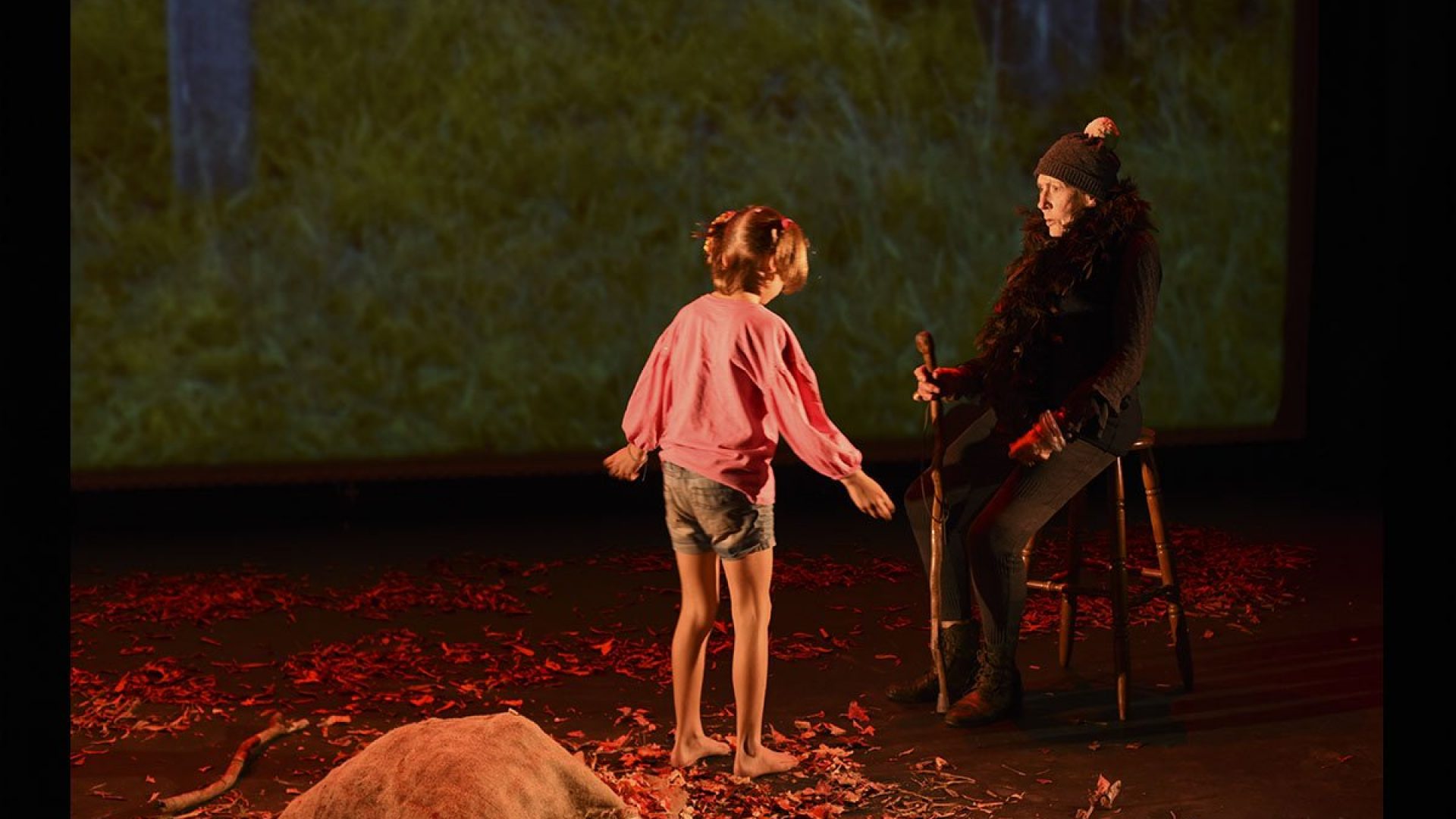 A person sitting on a stool on a stage. A child is standing in front of them