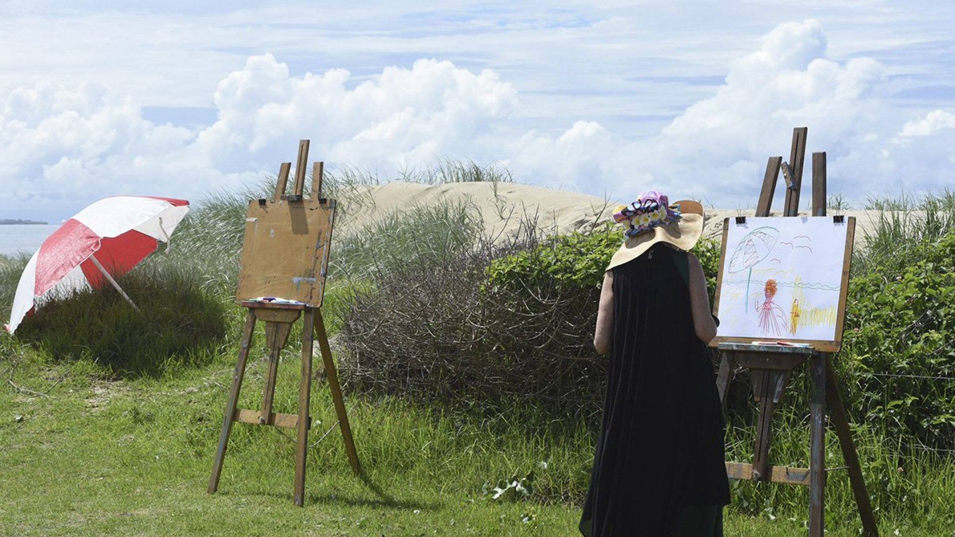 A person standing on a beach drawing on a easel