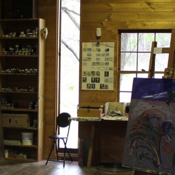 Artist studio with a tall window and a shelf with tubes of paints