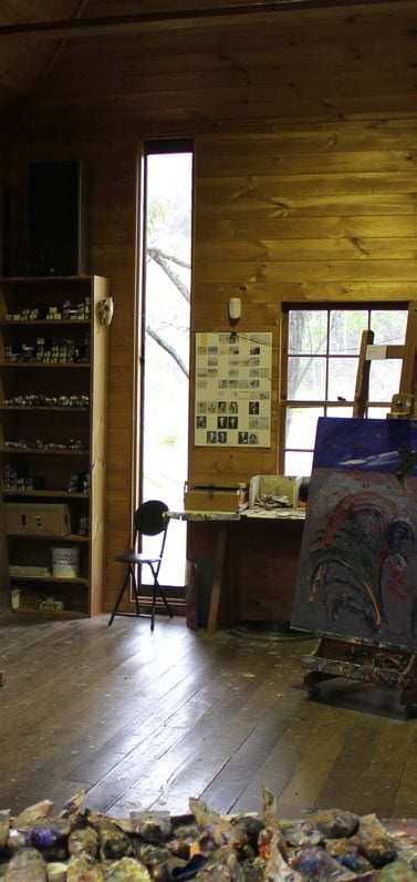 Artist studio with a tall window and a shelf with tubes of paints