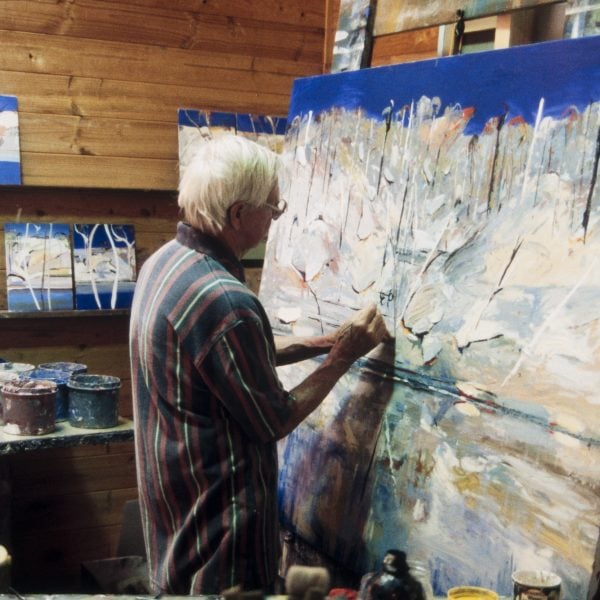 Person with short white hair paints a large abstract landscape painting