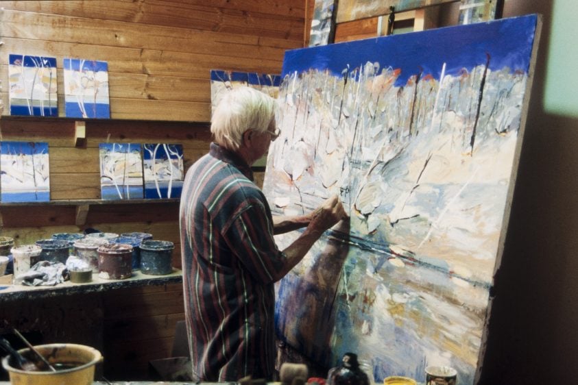 Person with short white hair paints a large abstract landscape painting