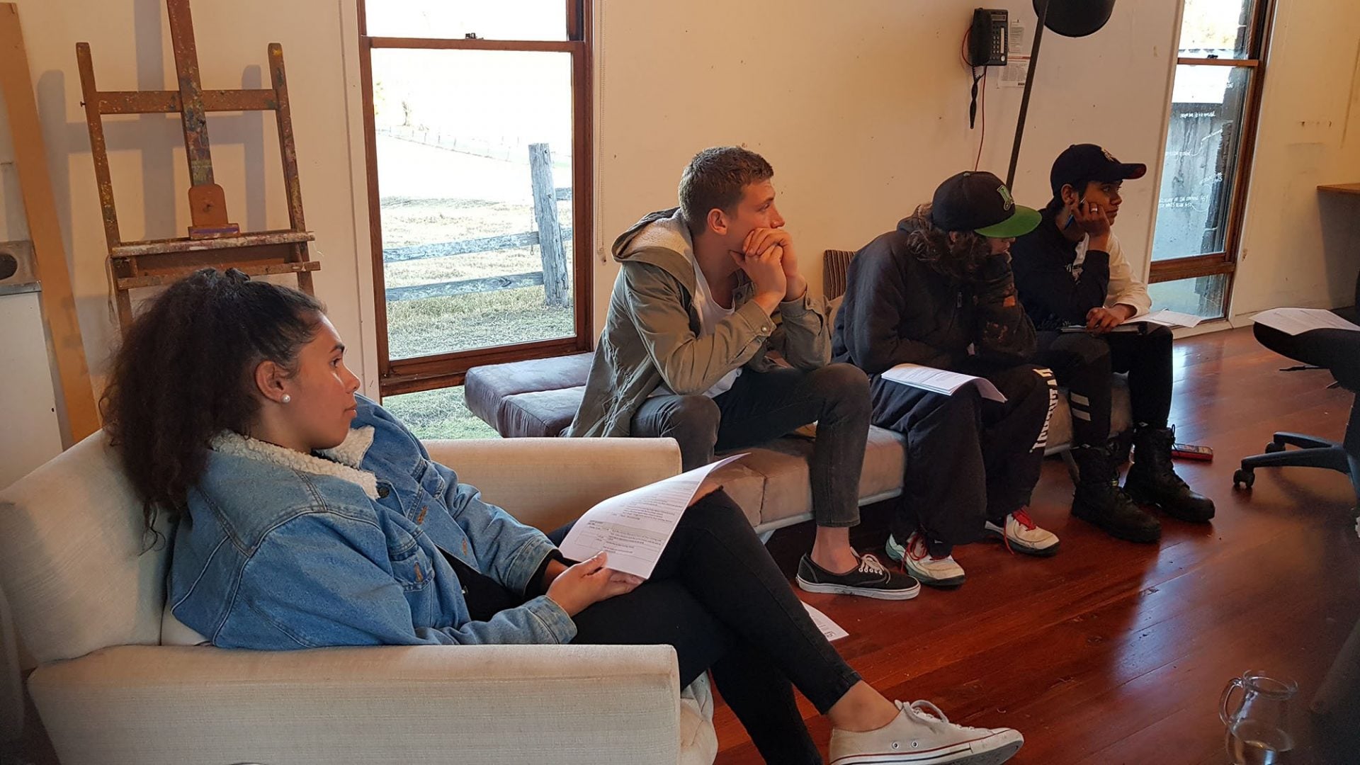 4 young people sitting on couches in a room. They're holding papers.