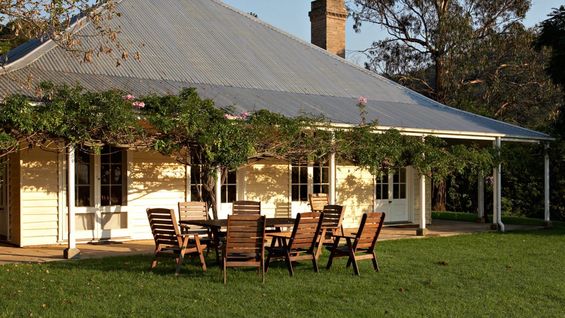 A small cottage building with large windows and a wooden table setting outside.