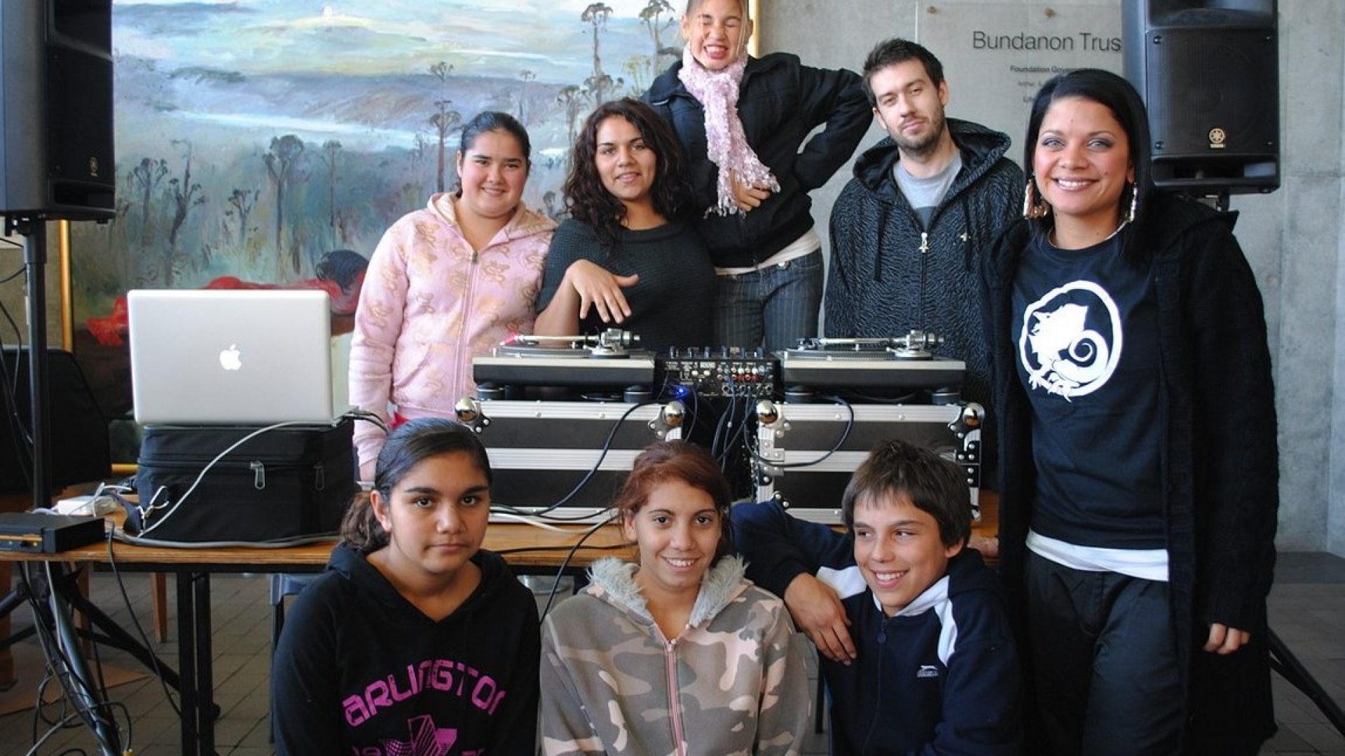 8 people standing around a DJ mixing desk