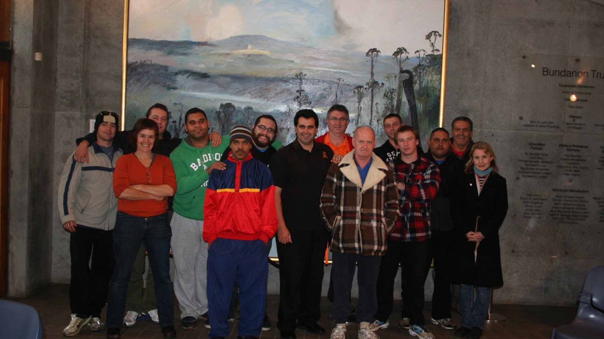 16 people stand together in front of a large landscape painting