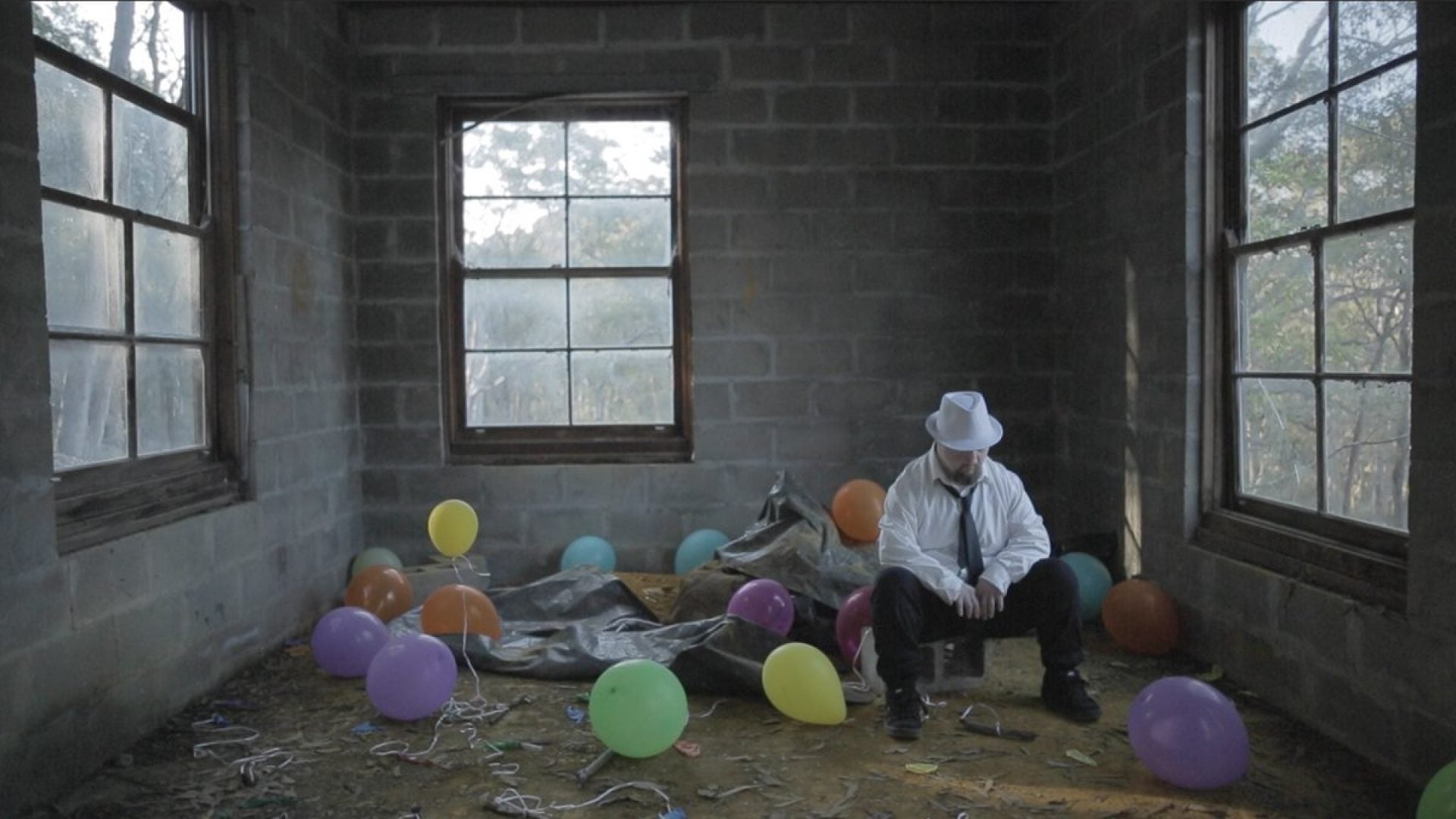 Person sits on a concrete block in an empty room with balloons on the ground