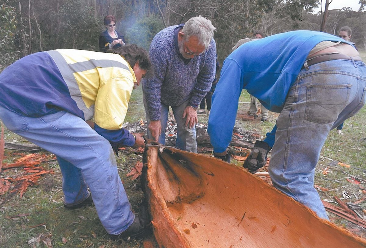 3 people building a small wooden canoe structure