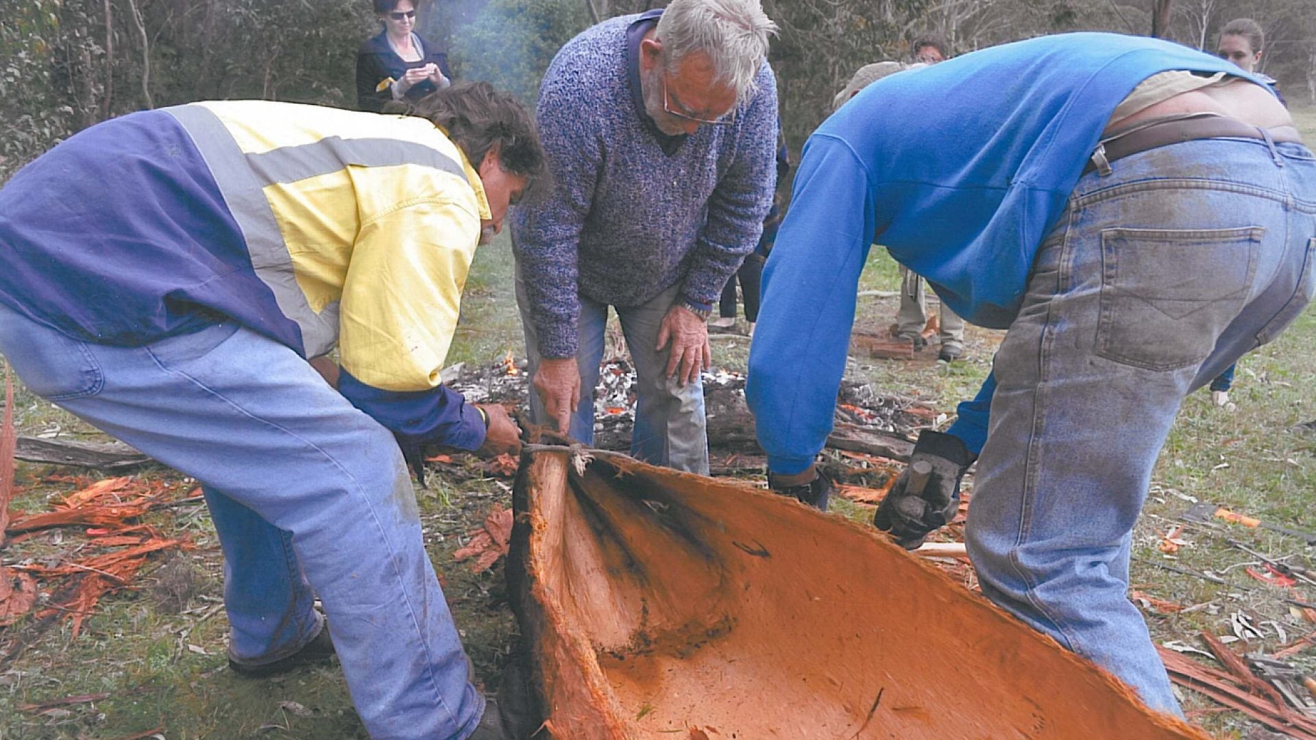 3 people building a small wooden canoe structure