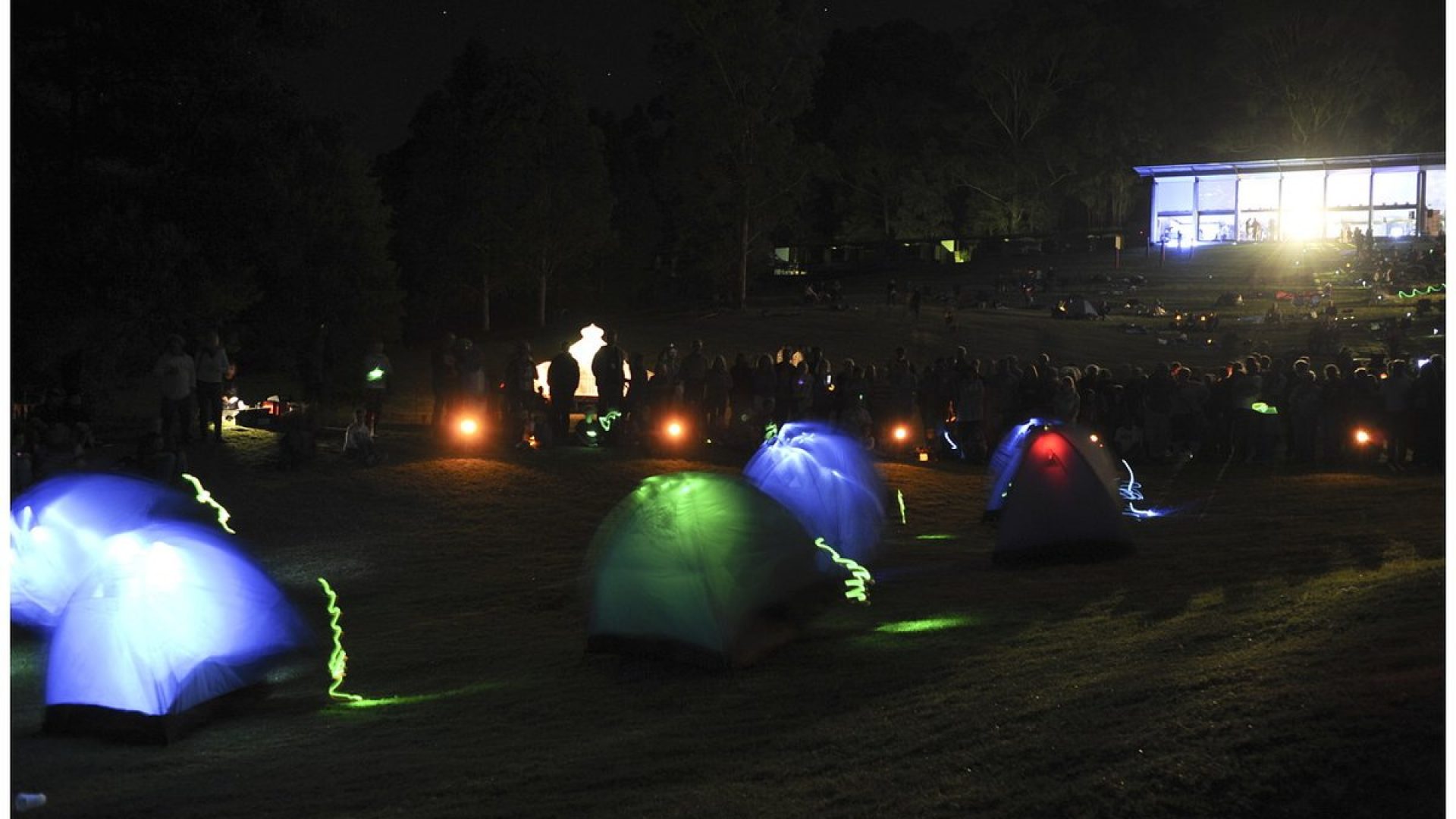 Hundreds of people sitting on grassy hills illuminated by small lights