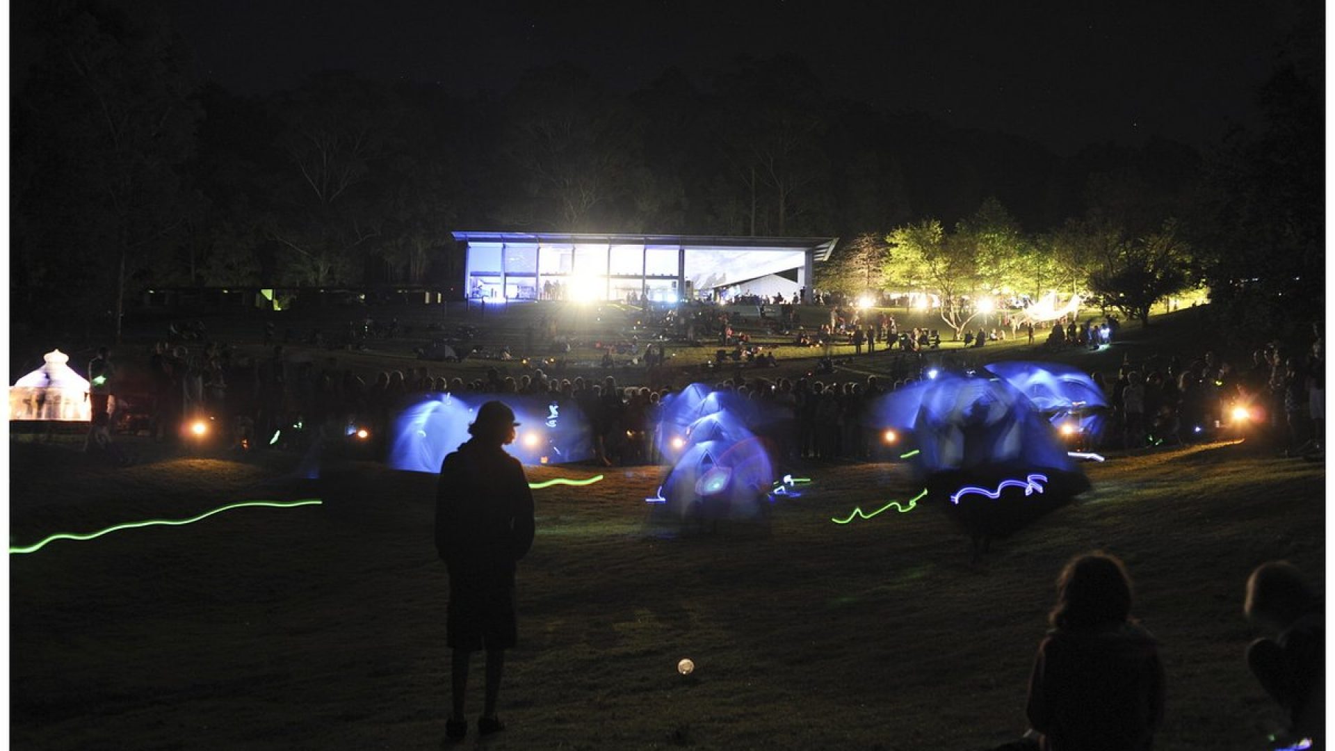 Hundreds of people sitting on grassy hills illuminated by small lights