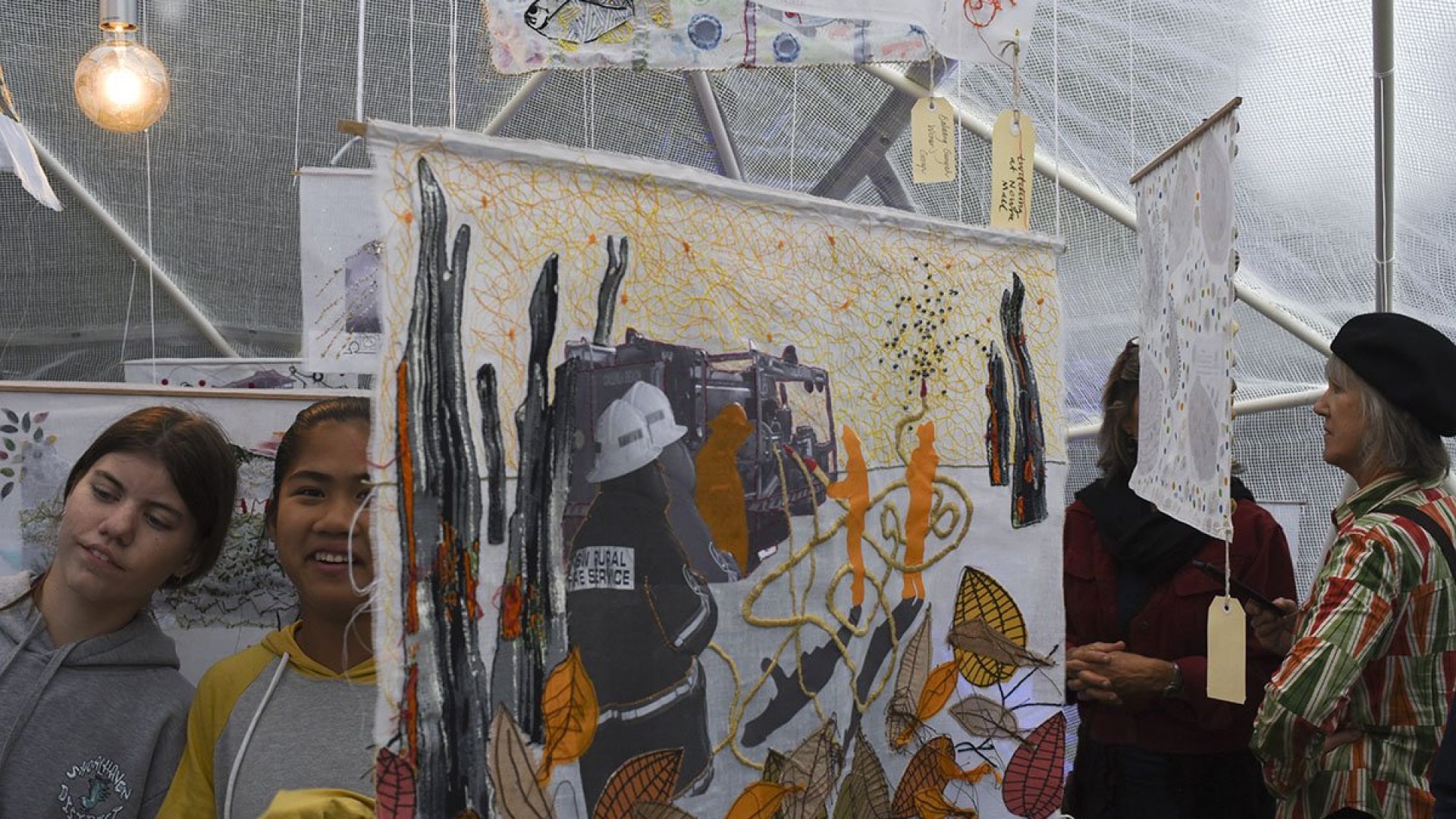 People standing in a small room that has artworks hanging from the ceiling