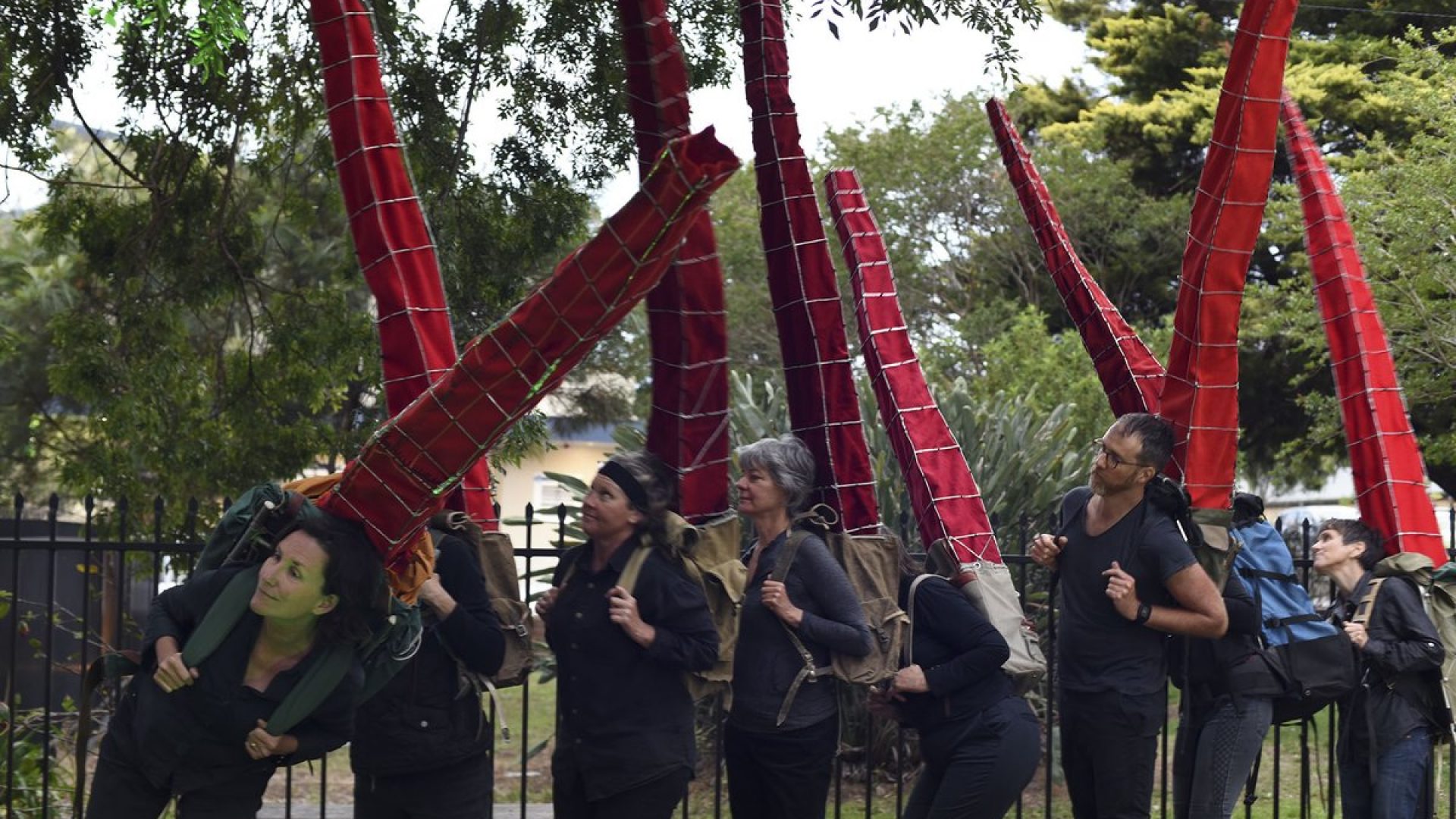 8 people standing in a line with very tall red backbacks on