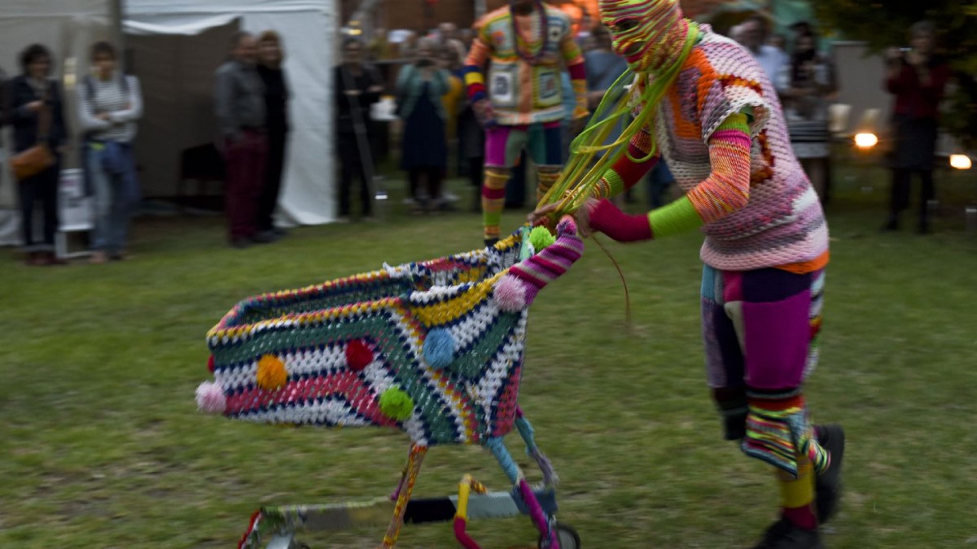 A person wrapped in knitted material pushing a trolley covered in knitting