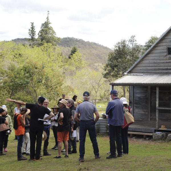A group of 15 people standing in front of a small wooden hut