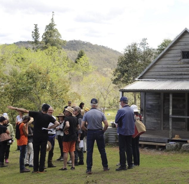 A group of 15 people standing in front of a small wooden hut