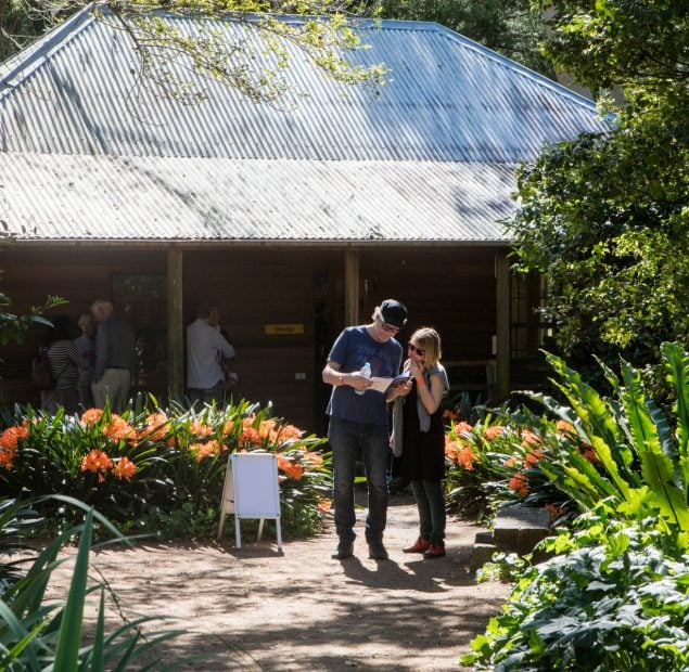 2 people standing in a garden with a wooden cottage building behind them