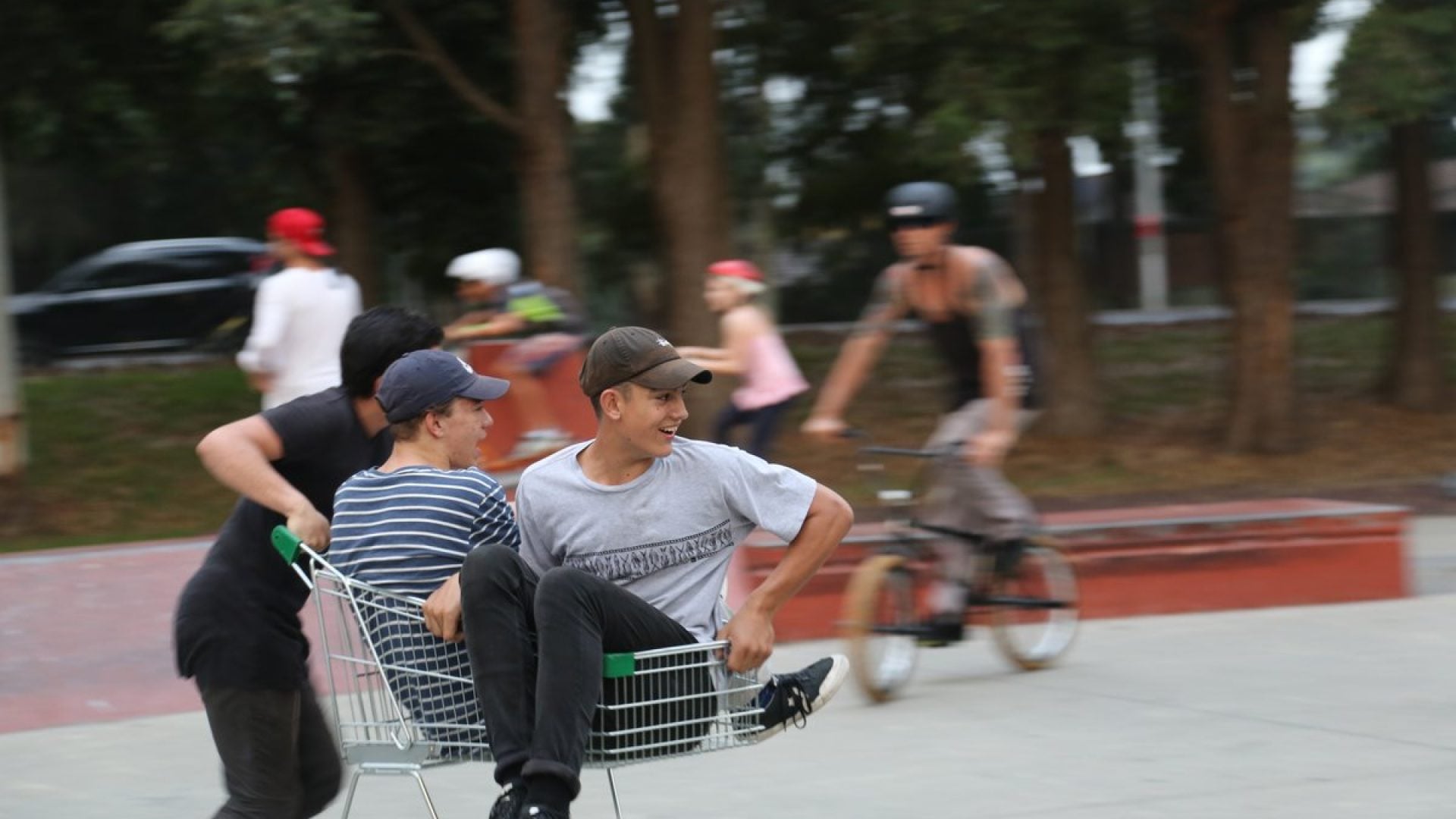 Two young people playing around in a shopping trolley at a skate park