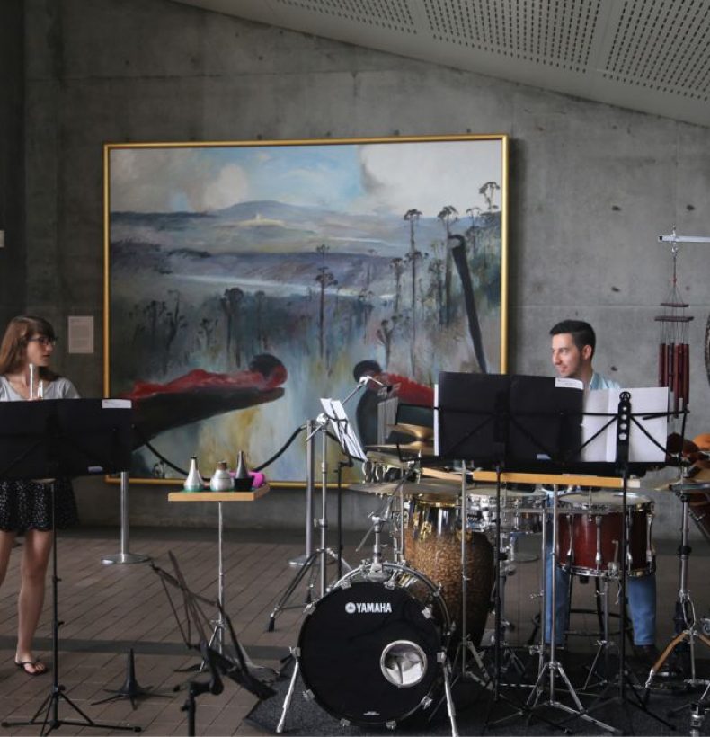 2 musicians in a room, one person is sitting at a large drum kit