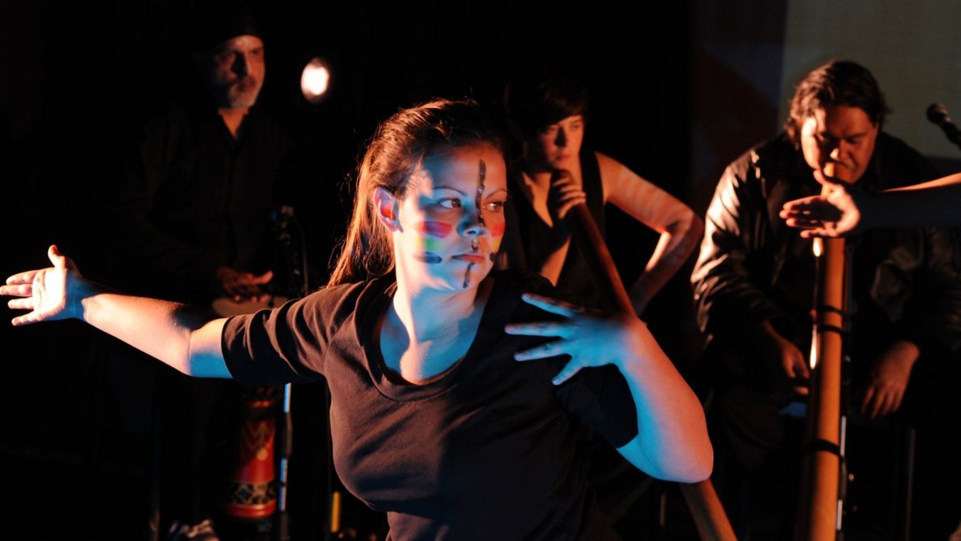 Person dancing with 3 didgeridoo players behind them