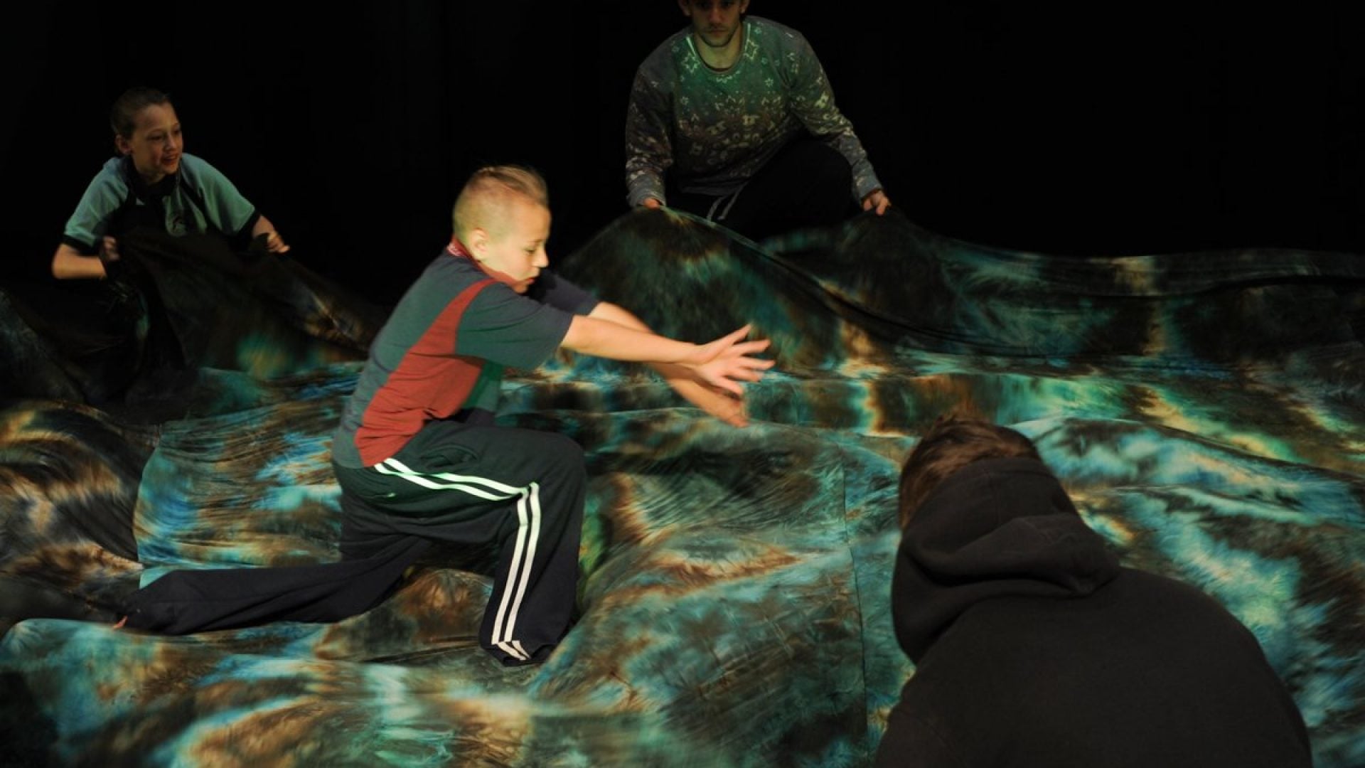 4 people dancing on stage with a large piece of green material