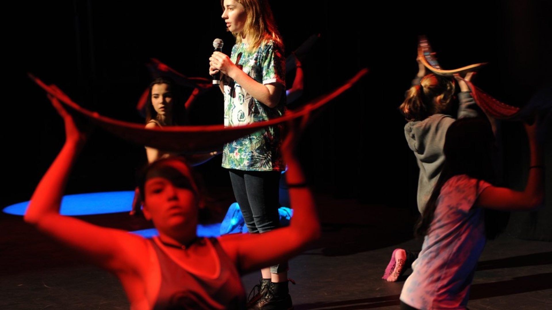 Person on stage with a microphone surrounded by 5 dancers